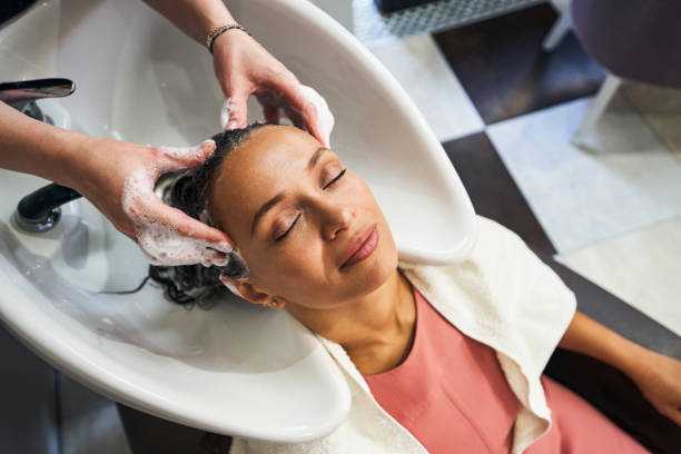 relaxed international woman closing her eyes while hairdresser washing her hair